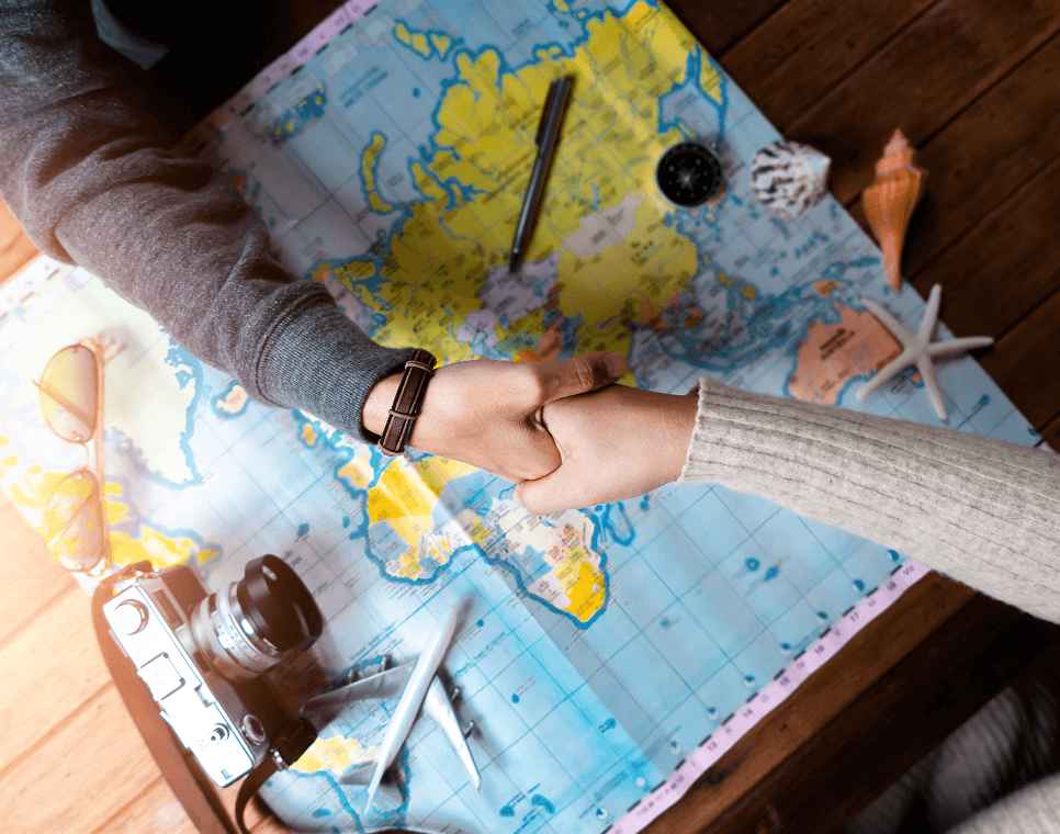 Consultants shaking hands over a world map with travel items